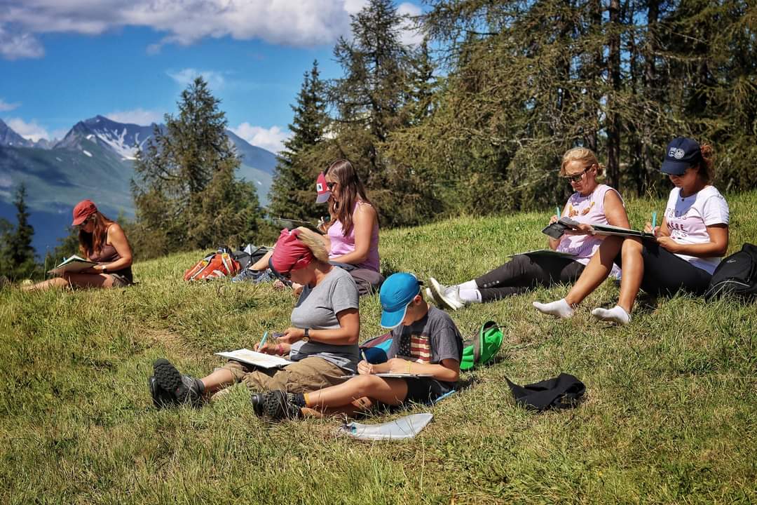 Participants à l'atelier balade aquarelle, assis dans un alpage face aux montagnes